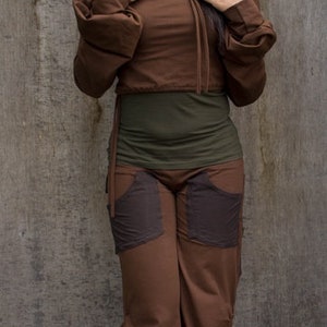 May include: A woman wearing a brown hooded top with a drawstring and matching brown pants. The pants have large pockets on the front.