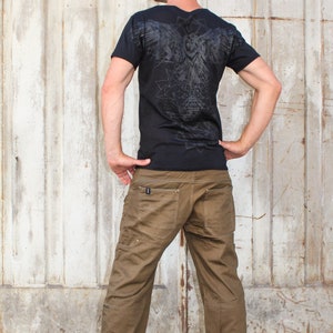 May include: A black t-shirt with a graphic print of an owl and geometric shapes on the back. The person is wearing brown cargo pants.