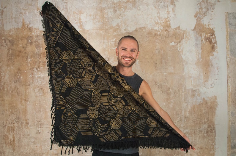 May include: A black triangular scarf with a gold geometric pattern. The scarf has a fringed edge.
