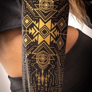 May include: Black and gold geometric patterned bag. The bag features a repeating design of diamonds, triangles, and lines. The bag is made of a soft material and is worn over the shoulder.