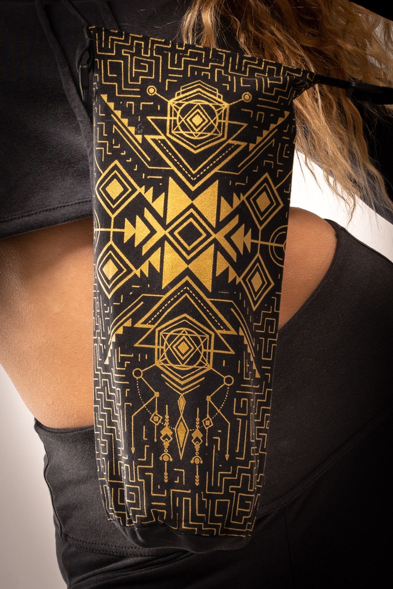 May include: Black and gold geometric patterned bag. The bag features a repeating design of diamonds, triangles, and lines. The bag is made of a soft material and is worn over the shoulder.