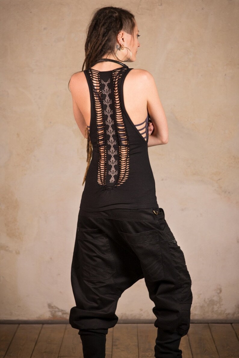 May include: Black tank top with a cut-out back design and decorative stitching. The model is also wearing black harem pants. The outfit is a unique style, perfect for casual wear or a music festival.