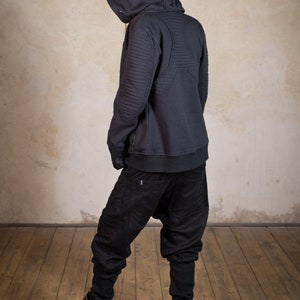 May include: A black hooded sweatshirt with a zipper closure and quilted detailing on the back. The sweatshirt is worn with black pants.