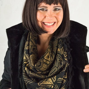 May include: A woman with dark brown hair wearing a black jacket with a gold and black geometric patterned scarf.