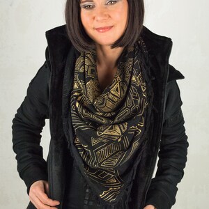 May include: A woman wearing a black hooded jacket with a black and gold geometric patterned scarf.