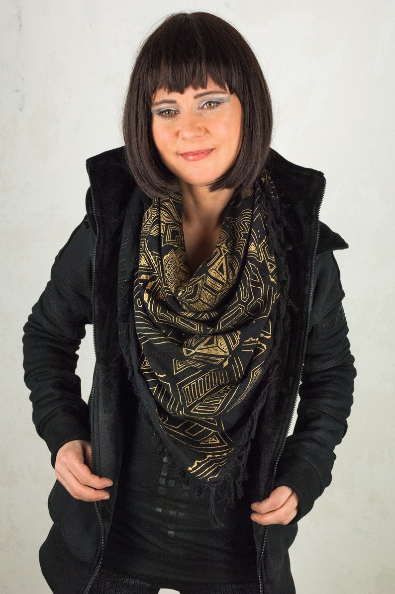 May include: A woman wearing a black hooded jacket with a black and gold geometric patterned scarf.