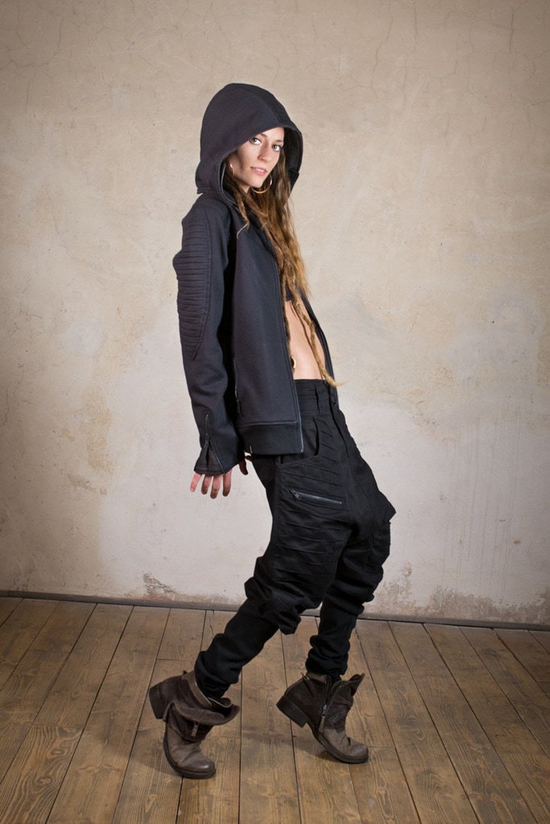 May include: A woman wearing a black hooded jacket with a zipper and a pair of black pants with a zipper detail. She is wearing brown boots.