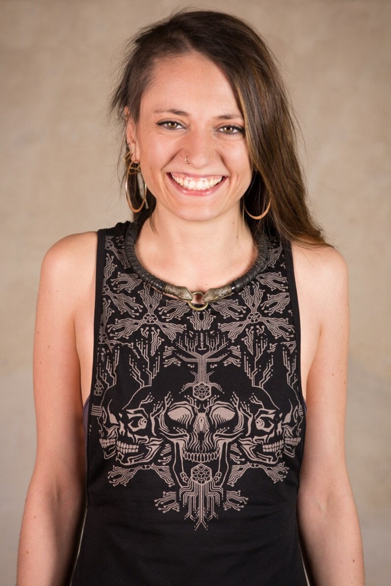 May include: Black tank top with a circuit board and skull design. The tank top has a round neckline and a sleeveless design. The model is wearing a black necklace with a circular pendant and gold hoop earrings.