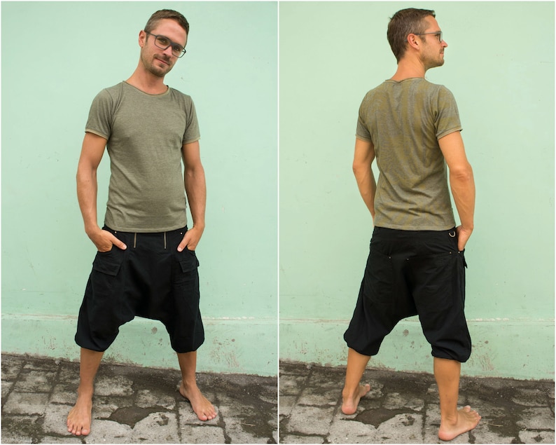 Op de afbeelding: Een persoon draagt een groen T-shirt en een zwarte cargo broek met een trekkoord. De broek heeft een uniek ontwerp met een grote zak aan de voorkant.