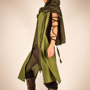 May include: A woman wearing a green hooded cloak with brown leather boots. The cloak is tied at the neck and has a long, flowing design. The boots are laced up and have a rugged look.