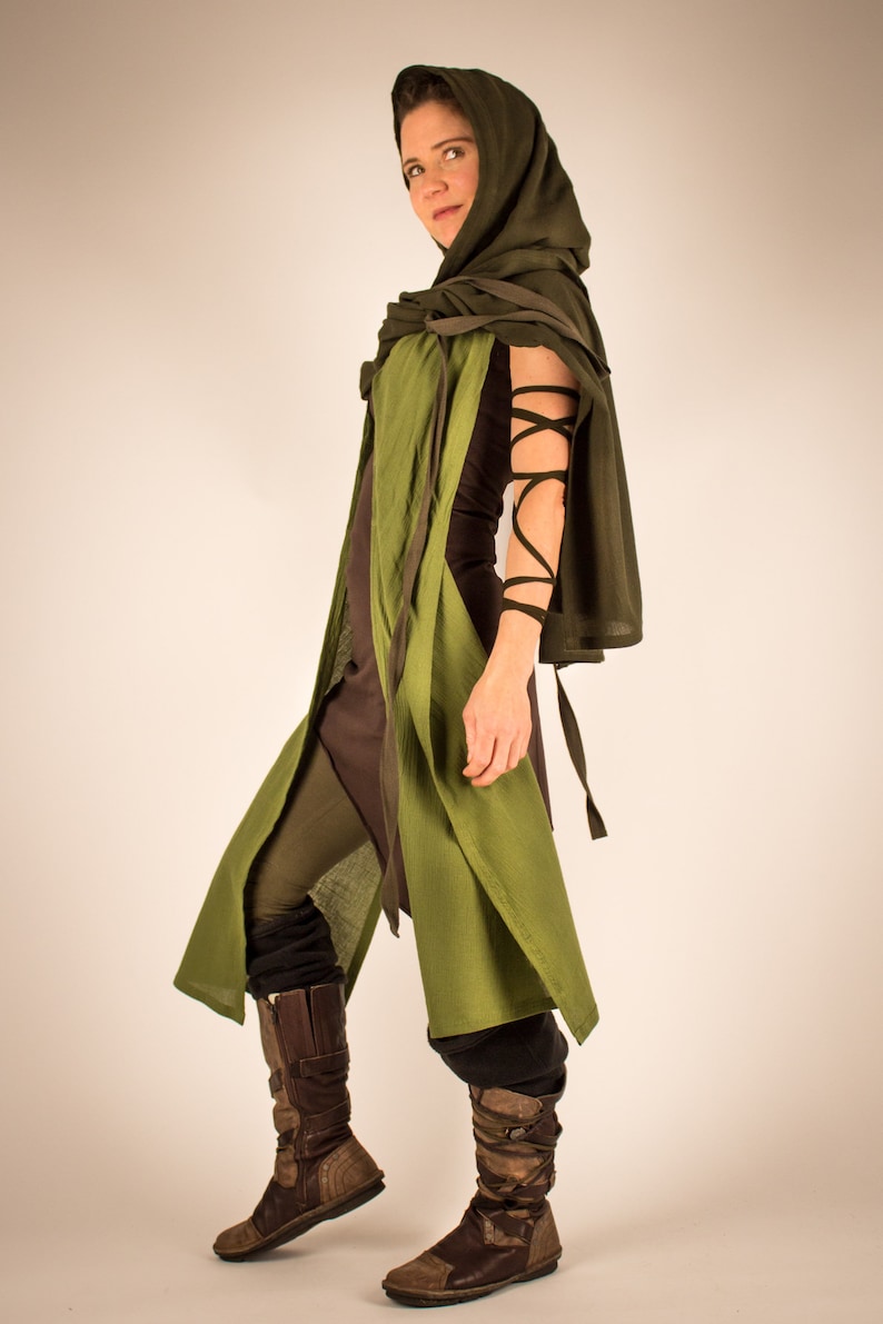 May include: A woman wearing a green hooded cloak with brown leather boots. The cloak is tied at the neck and has a long, flowing design. The boots are laced up and have a rugged look.