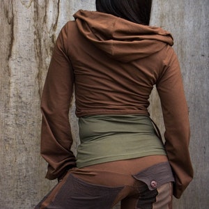 May include: A brown hooded jacket with long sleeves and a brown and green waistband. The jacket is worn over brown pants with a patchwork design.