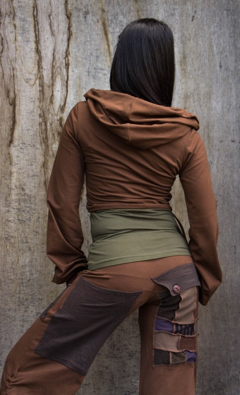 May include: A brown hooded jacket with long sleeves and a brown and green waistband. The jacket is worn over brown pants with a patchwork design.