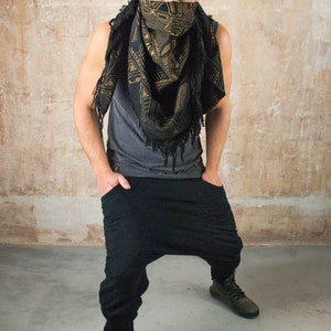 May include: A man wearing a black and gold patterned bandana over his face, a gray tank top, black pants, and black shoes.