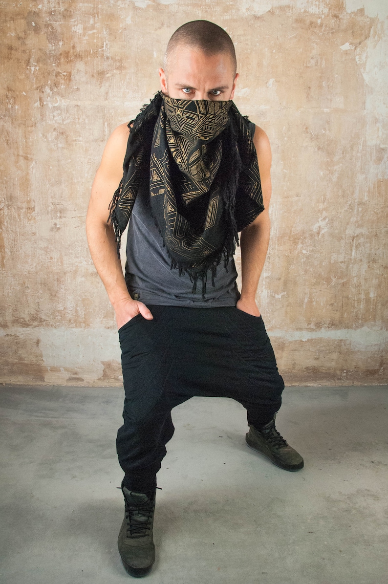 May include: A man wearing a black and gold patterned bandana over his face, a gray tank top, black pants, and black shoes.
