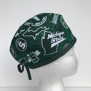 Peut inclure: Un bonnet de chirurgien vert avec un logo de l'Université d'État du Michigan et une carte du Michigan. Le bonnet est de couleur verte et blanche et a une cravate à l'arrière.