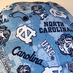 May include: Blue and white fabric with a repeated pattern of the University of North Carolina Tar Heels logo, the words "North Carolina" and "UNC", and a cartoon ram mascot. The fabric also features a blue footprint.