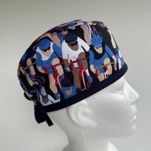 May include: A blue, white, and red patterned surgical scrub hat with a navy blue trim. The pattern features a group of cyclists in a race.