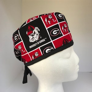 May include: Black and red surgical scrub hat with a repeating pattern of the University of Georgia bulldog mascot and the letter G.