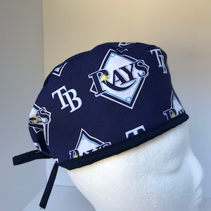 May include: A navy blue surgical scrub hat with a white and yellow Tampa Bay Rays logo and the letters "TB" repeated throughout the fabric.
