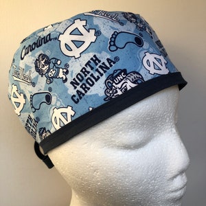 Könnte beinhalten: Eine blaue und weiße gemusterte OP-Mütze mit dunkelblauem Besatz. Die Mütze zeigt das Logo der University of North Carolina Tar Heels und die Worte "North Carolina".