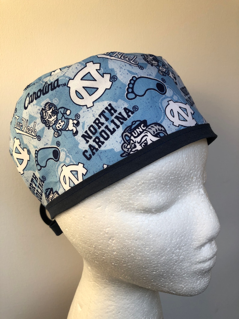 May include: A blue and white patterned surgical scrub hat with a navy blue trim. The hat features the University of North Carolina Tar Heels logo and the words "North Carolina".