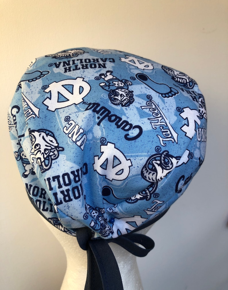 May include: A blue and white patterned surgical scrub hat with a navy blue tie. The hat features the University of North Carolina Tar Heels logo and mascot, Rameses.