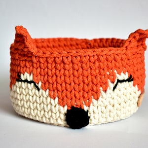 Op de afbeelding: Oranje en witte gehaakte mand in de vorm van een vos met zwarte ogen en een zwarte neus.