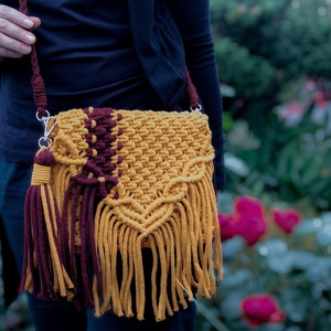 May include: A mustard yellow and burgundy crocheted crossbody bag with long fringe tassels.