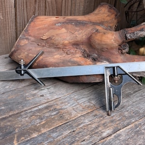 May include: A metal combination square tool featuring a long steel ruler with imperial markings up to 18 inches, paired with a black cast iron square head and a center head attachment, both secured with knurled brass adjustment nuts.