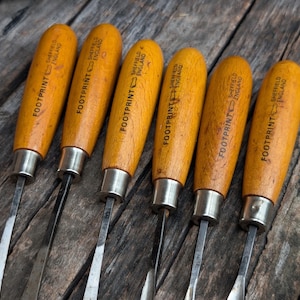 May include: A set of six wood carving chisels with light brown wooden handles. Each handle features a metal ferrule and is stamped with the text FOOTPRINT SHEFFIELD ENGLAND and a footprint logo. The metal blades extend from the handles.