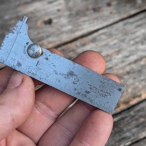 May include: A vintage metal marking gauge with inch measurements. The gauge is marked with the numbers 1 and 2, and the text "THE JENKINS RULE CO. WATERBURY, CONN. U.S.A." is visible. The gauge is held in a hand.