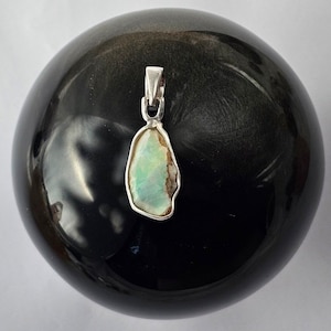 May include: A silver pendant featuring a light green opal stone with a rough, irregular shape.
