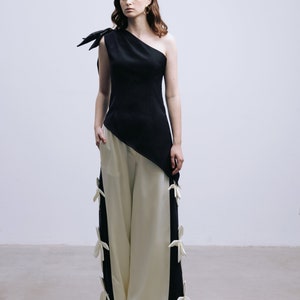 May include: A woman wearing a black one-shoulder top with a white and black asymmetrical pants. The pants have white bows on the sides.