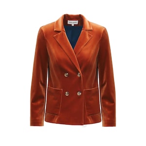 Può includere: Un blazer doppiopetto arancione bruciato con due file di bottoni e due tasche anteriori. Il blazer ha un risvolto a lancia e una fodera blu scuro. Il tessuto sembra essere velluto.