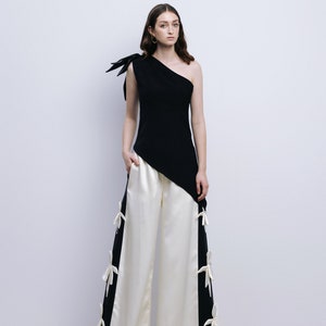 May include: A woman wearing a black one-shoulder top with a white bow detail and white wide-leg pants with black side panels and white bow details.