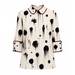 May include: Cream-colored coat with a black splatter design. The coat features a rounded collar and three-quarter sleeves with burgundy trim on the collar and cuffs. The coat has a button-up front.