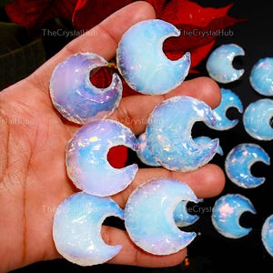 May include: Several opalescent crescent-shaped crystals. The crystals are a mix of blue, purple, and white, with a translucent appearance. They are smooth and polished. The background is dark, which accentuates the crystals' colours. The crystals are likely for decorative purposes.