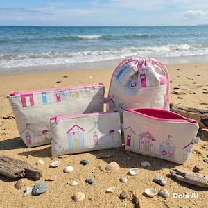 May include: A selection of beach-themed bags and pouches on a sandy beach. The bags display a pattern of colourful beach huts with pink, blue, and yellow accents. A drawstring bag and several zippered pouches are visible.