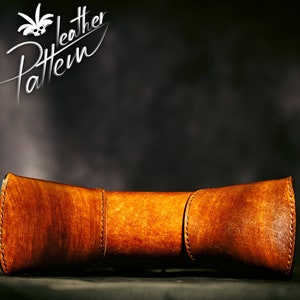 May include: A brown leather tube with stitching detail. The tube is curved and has a rounded shape. The tube is on a dark background.