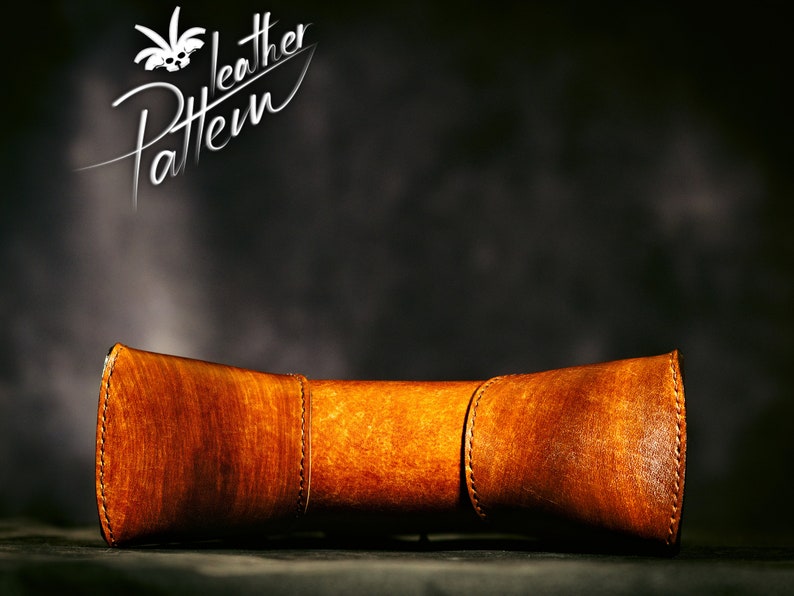May include: A brown leather tube with stitching detail. The tube is curved and has a rounded shape. The tube is on a dark background.
