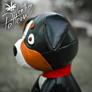 May include: A black, brown, and white leather dog toy with a red collar. The toy is made to look like a Bernese Mountain Dog.
