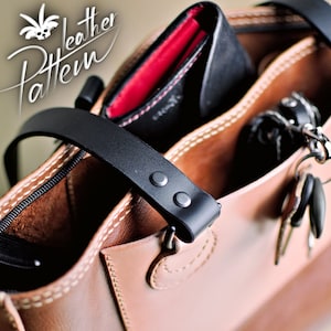 Puede incluir: Un bolso de cuero color canela con correas de cuero negro aseguradas con remaches plateados, un compartimento con cremallera negra y un bolsillo abierto que contiene una cartera negra con forro rojo y llaves. El texto dice Leather Pattern.