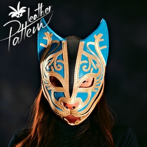 Peut inclure: Un masque de chat bleu et or avec des détails complexes. Le masque est en cuir et a une doublure noire. Le masque est porté par une personne aux longs cheveux bruns.