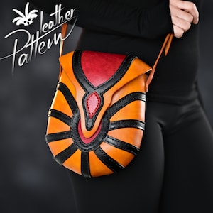 Puede incluir: Un pequeño bolso bandolera de cuero naranja, negro y rojo con un diseño geométrico. El bolso tiene un cierre de solapa y una correa larga.