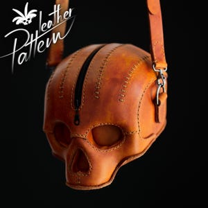K&ouml;nnte beinhalten: Eine hellbraune Ledertasche in Form eines menschlichen Sch&auml;dels mit einem zentralen schwarzen Rei&szlig;verschluss, sichtbaren N&auml;hten entlang der Kanten und einem Leder-Schulterriemen mit Metallbeschl&auml;gen. Der Text "Leather Pattern" ist oben links zu sehen.