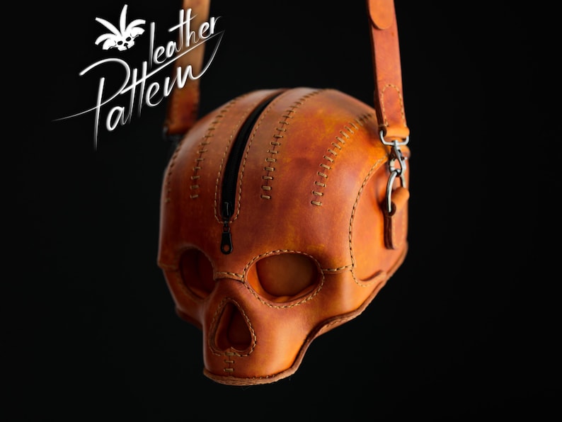 K&ouml;nnte beinhalten: Eine hellbraune Ledertasche in Form eines menschlichen Sch&auml;dels mit einem zentralen schwarzen Rei&szlig;verschluss, sichtbaren N&auml;hten entlang der Kanten und einem Leder-Schulterriemen mit Metallbeschl&auml;gen. Der Text "Leather Pattern" ist oben links zu sehen.