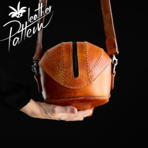 K&ouml;nnte beinhalten: Eine hellbraune Lederschultertasche mit abgerundeter, strukturierter Form und einem zentralen vertikalen Rei&szlig;verschluss. Die Tasche weist sichtbare Ziern&auml;hte entlang der Kanten und einen langen Lederriemen auf. Der Text "Leather Pattern" ist sichtbar.