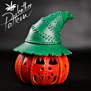 Puede incluir: Una calabaza de cuero hecha a mano con un sombrero de cuero verde. La calabaza tiene una cara de calabaza tallada.