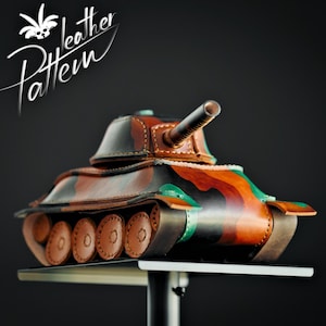 May include: A handcrafted leather tank model featuring a camouflage pattern in shades of brown, black, and green. The tank has a rotating turret, a prominent barrel, and detailed circular wheels along the sides. The text Leather Pattern is visible.